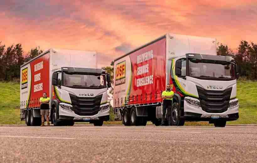 Two DSE Transport drivers standing with their Iveco S-Way curtainside trucks at sunset