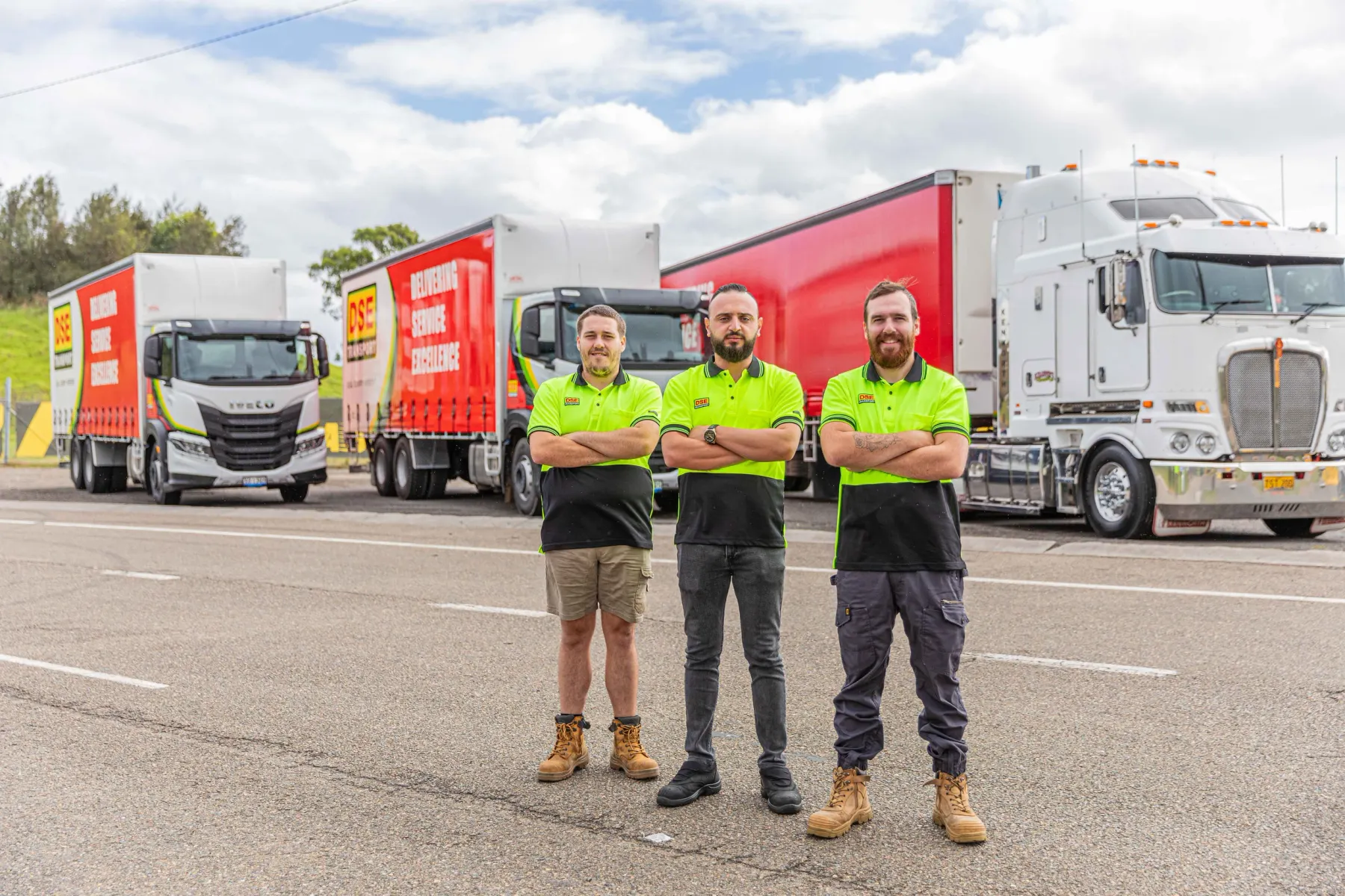 Three DSE Transport drivers in hi-vis uniform standing in front of DSE trucks