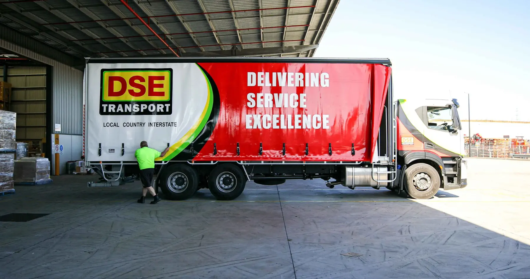 DSE Transport driver opening the side curtain of a tautliner to unload crated freight